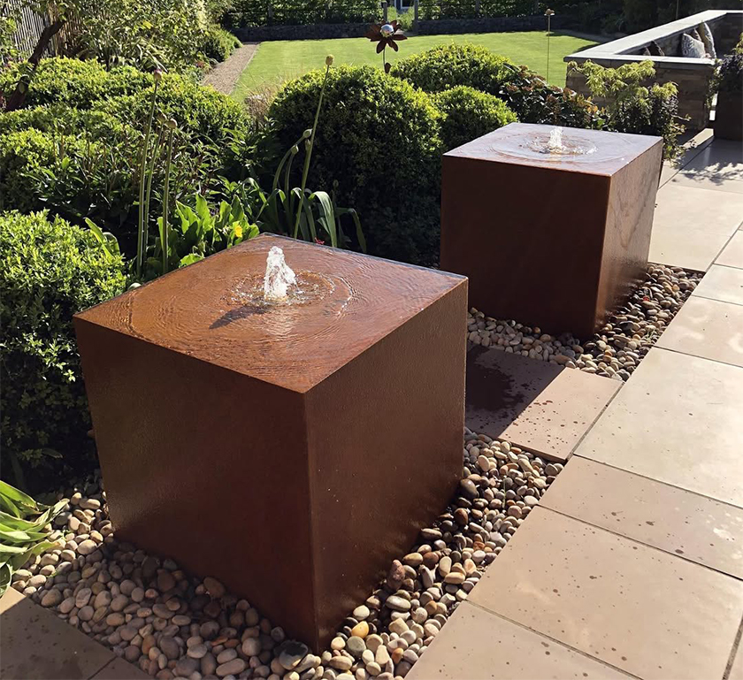 Fontaines cubiques en acier Corten Maroc installées dans un jardin contemporain avec galets décoratifs et végétation