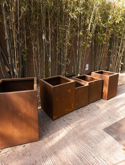 Ensemble de jardinières en acier Corten Maroc installées devant une haie de bambous dans un aménagement extérieur contemporain