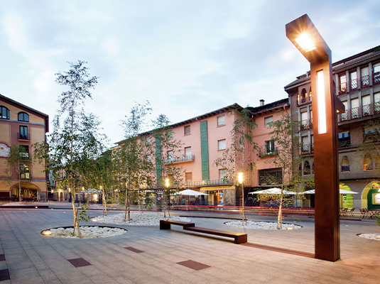 Luminaire urbain en acier Corten Maroc installé sur une place publique contemporaine avec banc et aménagement paysager