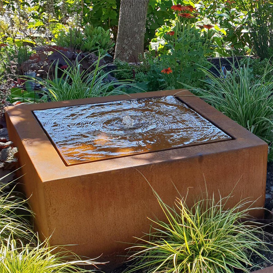 L’acier Corten utilisé pour une fontaine cubique installée dans un jardin paysager avec végétation décorative