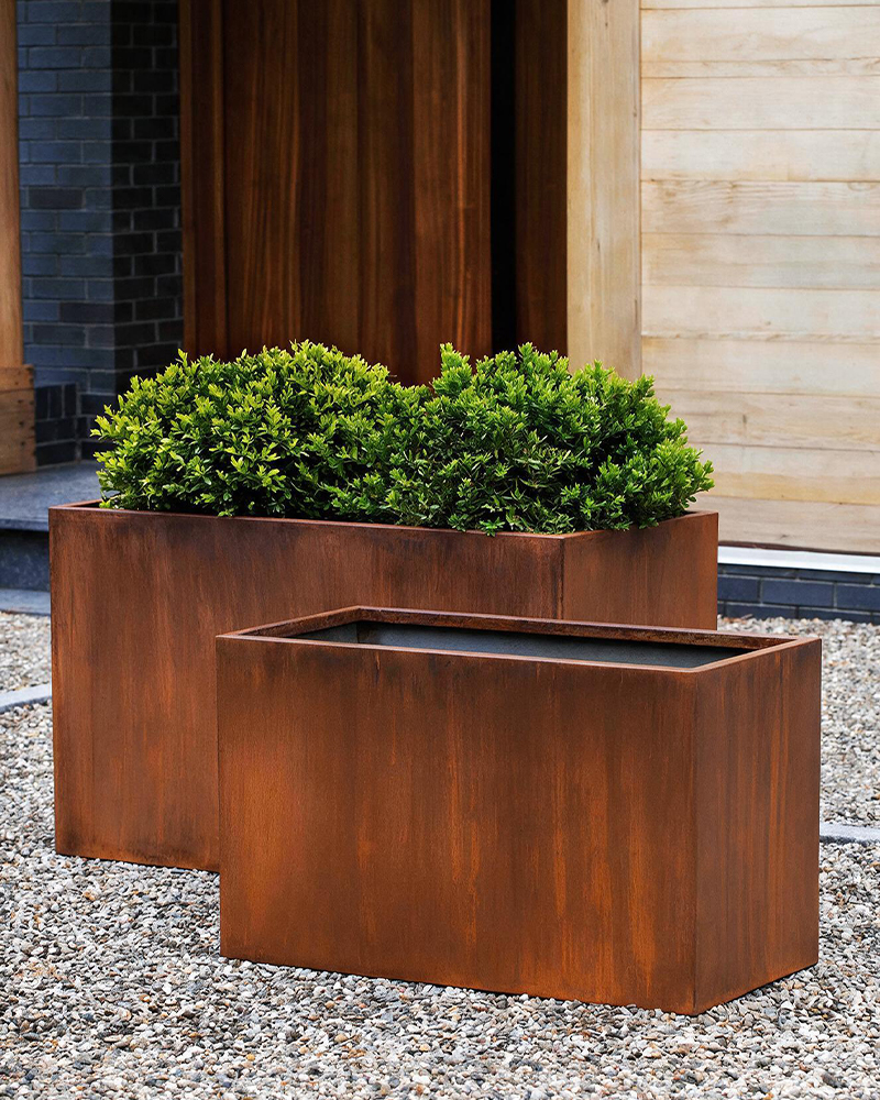 Deux jardinières rectangulaires en acier Corten Maroc installées devant une maison contemporaine avec arbustes décoratifs