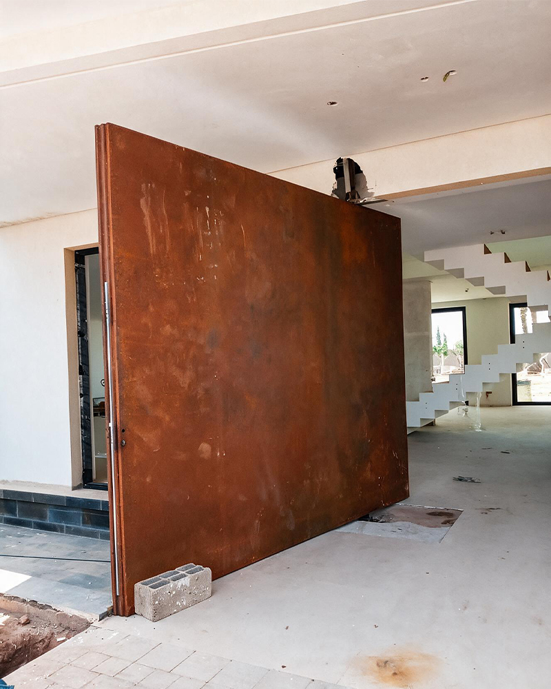 Grande porte pivotante en acier Corten Maroc installée à l’entrée d’une villa contemporaine en construction