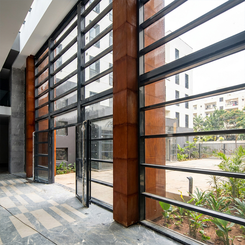 Projets en acier Corten avec habillage de poteaux métalliques autour d’une grande entrée vitrée contemporaine